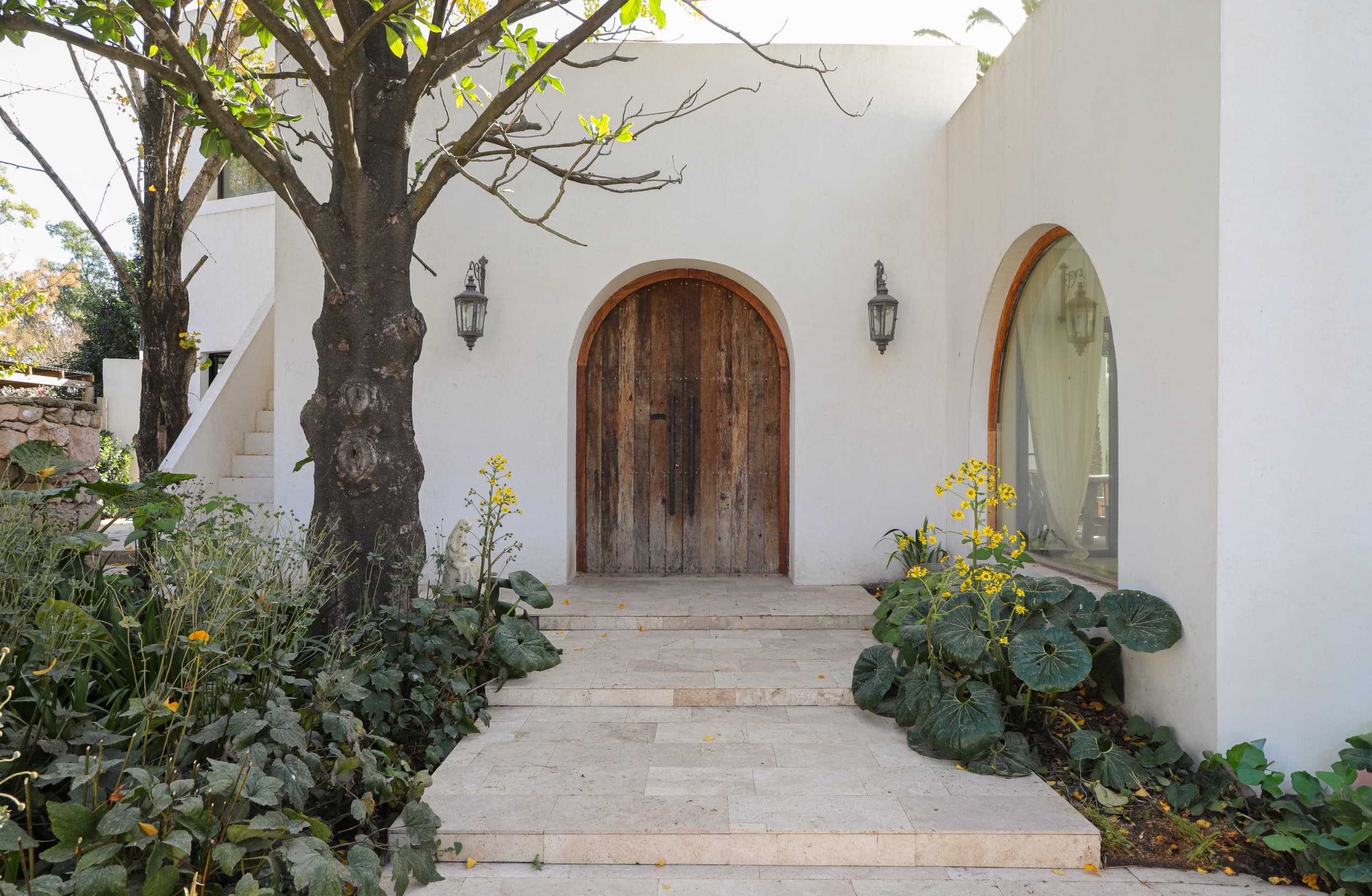 Entrada con puerta de madera en arco y vegetación
